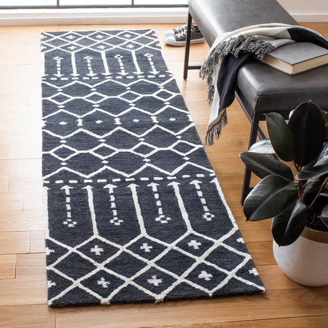 Safavieh Himalaya Darin Geometric Area Rug runner featuring black and white geometric diamond and linear patterns, crafted from 100% hand-loomed wool, shown on a light hardwood floor beside a black leather bench with a fringed throw and book, near a potted plant, ideal for modern entryways or hallways.