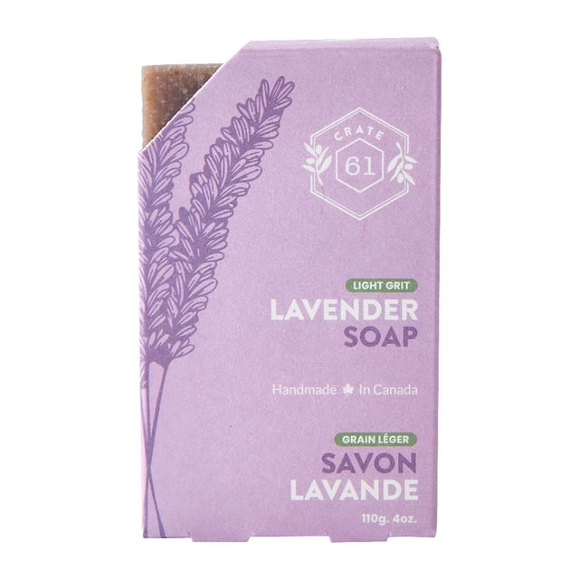 Lavender Natural Bar Soap | 110g by Crate 61 Organics Inc, front view of a partially unwrapped rectangular bar soap with light brown texture, wrapped in lavender-colored packaging featuring lavender sprig illustrations and bilingual text indicating light grit and handmade in Canada, ideal for soothing skin and calming the mind.