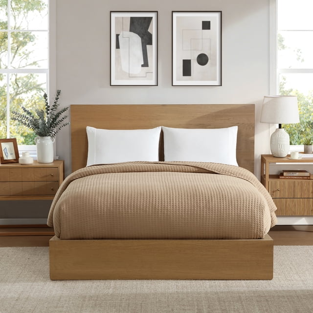 Allswell Couverture, Beige, Grand Lit sur un Lit Plateforme en Bois avec une Tête de Lit Rectangulaire, avec Tissu Froissé en Coton Texturé et Rembourrage en polyester Peluche. la Couverture Beige Couvre le Lit avec Deux Oreillers Blancs. la Chambre Comprend des Tables de Nuit en Bois avec un vase Blanc de Verdure et une Lampe en Céramique, des Murs Neutres avec Deux Oeuvres d'Art Abstraites Encadrées, et de Grandes Fenêtres Montrant de la Verdure à l'Extérieur. la Couverture Est Idéale pour Superposer au Fil des Saisons et Est Livrée avec un Sac en Tissu Réutilisable.
