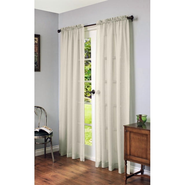 Loft Living Cannes Rod Pocket Linen-Like Single Curtain Panel Sheer 56" x 63" in Ivory hanging on a dark metal rod over a glass-paneled door in a kids' room with light grey walls, wooden floor, a metal chair with an open book, and a wooden cabinet, providing sheer daytime privacy while allowing natural light.