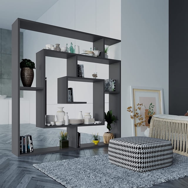 JV Home Labyrinth Collection 51x49 Inch Grand Bookcase in anthracite, featuring a modern geometric design with six-tier shelving. The bookcase is made from durable manufactured wood with a melamine coating, offering ample storage for books, decor, electronics, and houseplants. Displayed in a contemporary living room setting with decorative items and books arranged on the shelves. Assembly required.