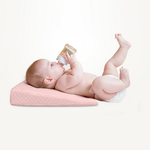 HomeNest Pillow Reflux Cushion Foam for Pram Cot Bed Flat Head shown in use, featuring a baby lying on the wedge pillow with a gentle incline of 12–15 degrees. The pillow is made of high-density memory foam with a breathable cotton cover in a soft pink color. Designed to promote better sleep by elevating the baby's head and torso, it provides ergonomic support and excellent air circulation. The cover is removable and machine washable for easy maintenance.