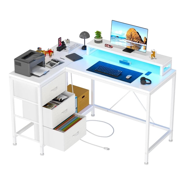 TROPOW Ergonomic L-Shaped Computer Desk in rustic brown and white, designed for gaming or home office use. Features a spacious corner layout with 4 power outlets, 2 USB ports, and 7-color LED lights for ambiance. Includes a removable computer stand, three fabric drawers, and a bookshelf for organized storage. The desk is shown with a monitor, keyboard, and accessories, emphasizing its functionality as a corner desk and LED gaming desk.