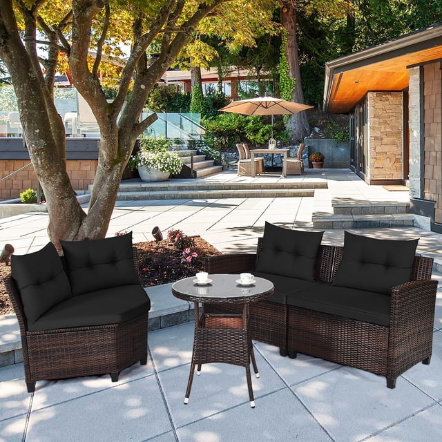 Costway 4PCS Outdoor Patio Rattan Furniture Set Cushioned Sofa Table Black displayed in a contemporary patio setting. This weather-resistant conversation set includes a left armrest chair, right armrest chair, middle sofa, and a round coffee table with tempered glass. Constructed with hand-woven rattan and sturdy steel, it features removable black cushions for added comfort and easy cleaning. Perfect for outdoor spaces like gardens, poolside, or backyards.