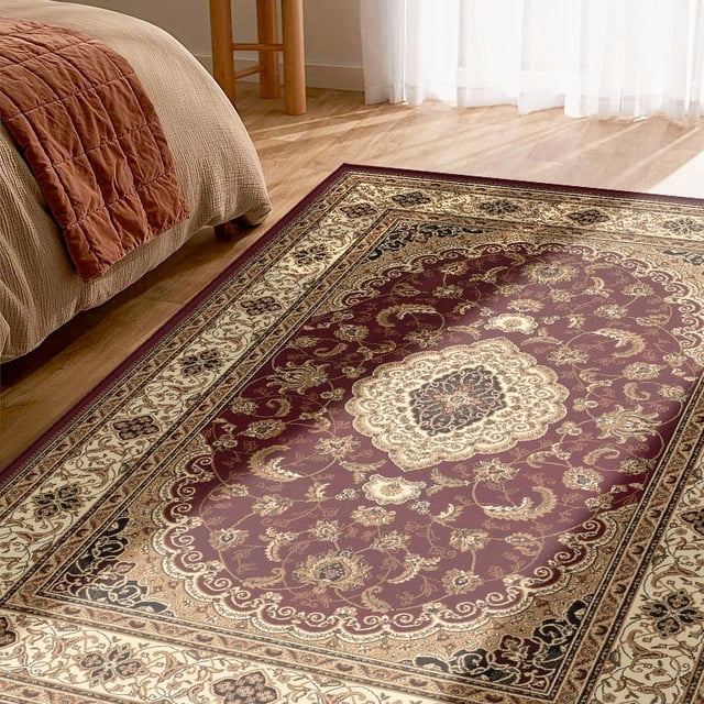 Rug Branch Majestic Collection Traditional Oriental Area Rug with intricate floral and scrollwork patterns in burgundy and cream, woven from 100% olefin heatset for stain and fade resistance, placed on a light hardwood floor beside a beige bed with a rust-coloured quilt, suitable for living rooms, bedrooms, and hallways.