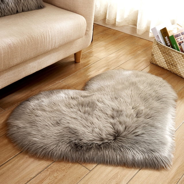TIMIFIS Rug Home Decor Wool Imitation Sheepskin Rugs Faux Fur Non Slip Bedroom Shaggy Carpet Mats Carpet - Fall. A heart-shaped faux fur area rug in a soft grey tone, placed on a wooden floor next to a beige sofa. Made of polyester, this shaggy rug offers a luxurious and eco-friendly design, suitable for bedrooms, living rooms, or as a seat cushion or yoga mat. Dimensions: 40 x 50 cm.