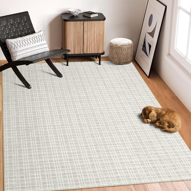 TROPOW washable checkered area rug with a modern plaid print, shown in a light neutral tone. Made from soft faux wool polyester fibers with a low pile height, this non-shedding rug features a TPR non-slip backing for stability. Ideal for indoor use in living rooms, bedrooms, dining rooms, or offices. The rug is displayed in a cozy, modern room with wooden flooring, a black chair, a small cabinet, and a dog resting on the rug.