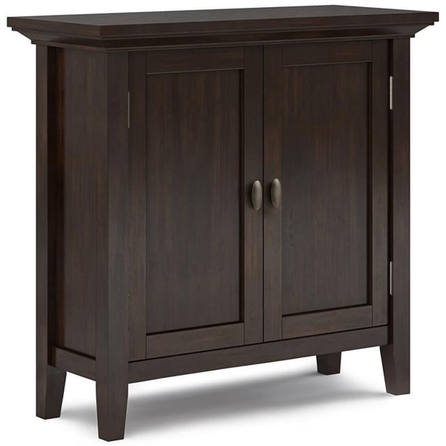 Redmond Solid Wood 32-inch wide transitional low storage cabinet in brunette brown. Crafted from hand-finished pine solid wood with a protective NC lacquer to enhance the grain. Features two doors with antique brass hardware, opening to adjustable shelves for versatile storage. Includes tapered legs and a molded crown-edged tabletop, ideal for use as an entryway cabinet, living room storage, or dining room organizer.