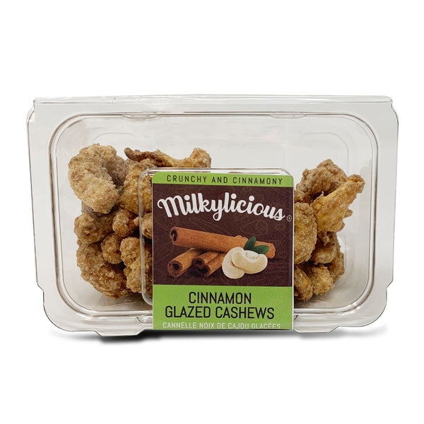 Milkylicious Cinnamon Glazed Cashews in a 4 oz clear plastic clamshell container. The label features the Milkylicious logo, cinnamon sticks, and cashews, highlighting the crunchy and cinnamon-flavoured snack. The cashews are visibly coated with a caramelized glaze, offering a sweet and nutty treat.