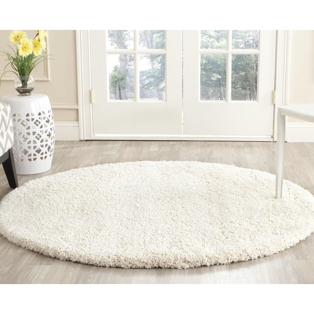 Safavieh Milan Harlow Solid Shag Area Rug, 5'1" round ivory rug with 2-inch thick synthetic shag pile, placed on light hardwood floor in a bright room with glass doors, ideal for high-traffic living areas and adding warm texture to modern décor.