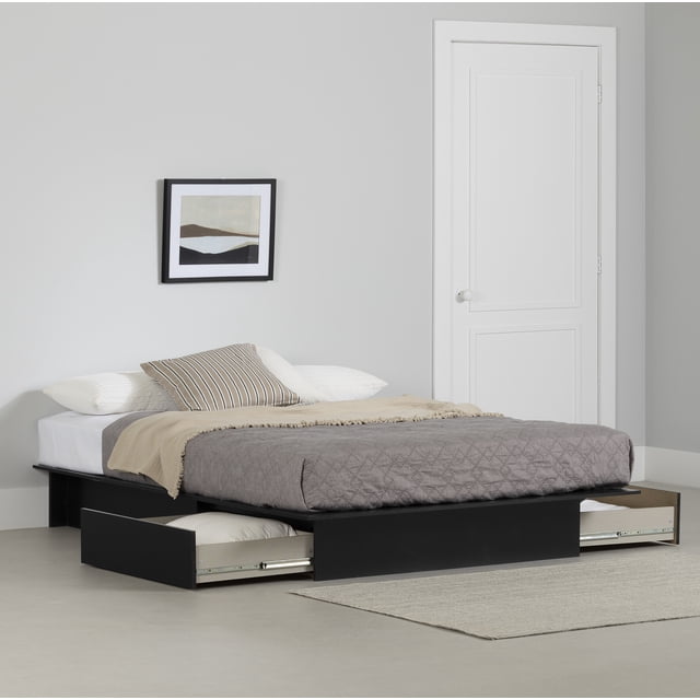 South Shore Step One Full/Queen Platform Bed with drawers in pure black, featuring two full-extension underbed storage drawers open on each side with pillows inside, a sturdy low-profile frame supporting a mattress with gray quilted bedding, beige throw, and striped pillow, set in a neutral bedroom with light gray walls, a framed abstract landscape, and a white door, suitable for maximizing bedroom storage space.