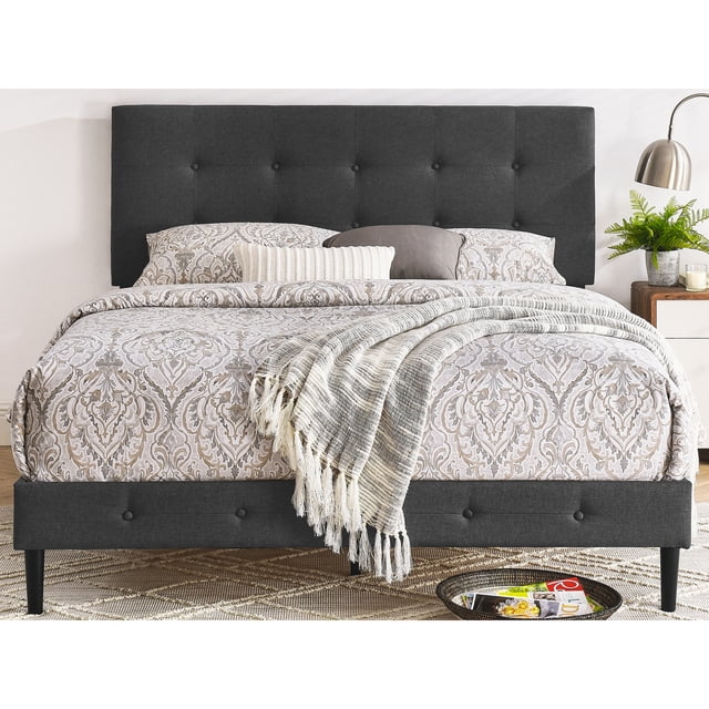 DeCoro Cambridge Cadre de Lit Plateforme en Bois Rembourré, Format Double, avec une Tête de Lit Capitonnée à Boutons Gris Foncé et des Lattes en Bois Durables. Conçu avec une Literie à Motifs et des Coussins Décoratifs, Il Complète le Mobilier de Chambre Moderne. le Cadre Comprend une table de Chevet avec une Lampe et de la Verdure.