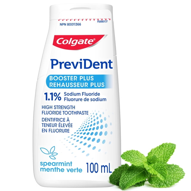 Colgate PreviDent Booster Plus High Fluoride Toothpaste, spearmint flavor, in a 100 mL white bottle with blue and red text highlighting 1.1% sodium fluoride for enamel repair and cavity protection, shown with fresh spearmint leaves.