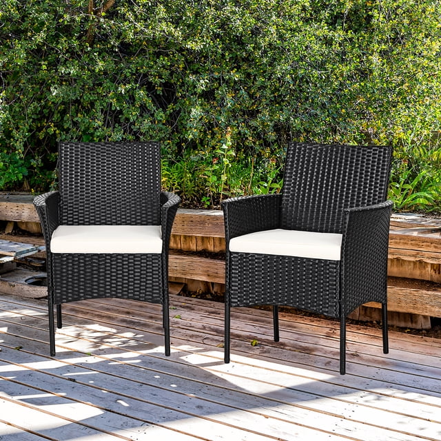 Costway 2PC Chairs Outdoor Patio Rattan Wicker Dining Arm Seat w/ Cushions. The set includes two black PE rattan chairs with gently sloping armrests and off-white removable seat cushions. Each chair measures 25” x 23” x 33” (L x W x H) and has a weight capacity of 360 lbs. The chairs are placed on a wooden deck with greenery in the background, ideal for patios, porches, or gardens.