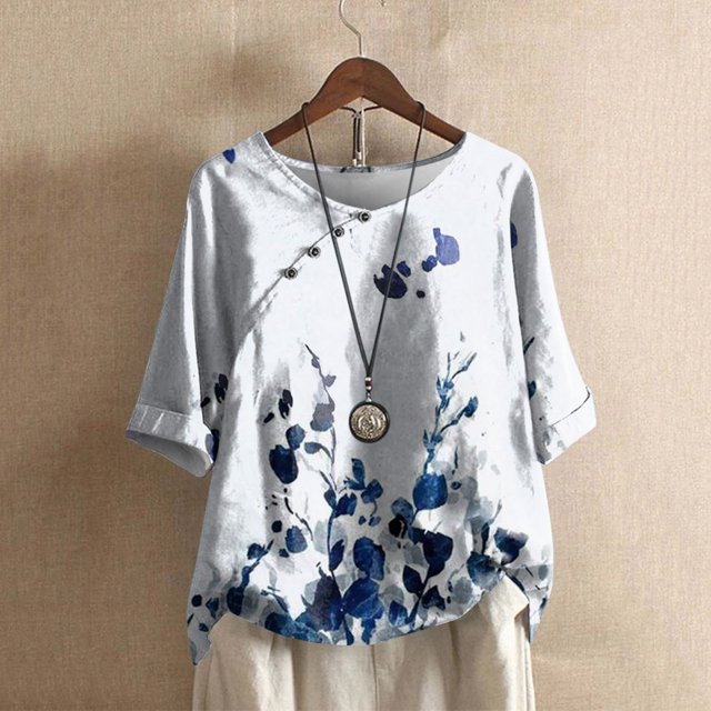 SMihono Hauts pour Femmes Été Chic Décontracté Mode Femme Décontracté Col Rond Blouse à Imprimé T-Shirt à Manches 1/2 Hauts d'Été T-Shirt Grande Taille. Cette Blouse Présente un Col Rond, des Manches Mi-Longues et un Imprimé floral Bleu sur un Fond Blanc. Fabriquée en polyester Léger, Elle Est Douce, Respirante et Idéale pour les occasions Estivales Décontractées Ou Chic. Exposée sur un Cintre avec un Collier Pendentif et un Pantalon beige, sur un Fond Neutre.