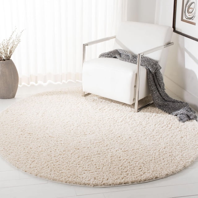 SAFAVIEH August Carlene Tapis à Poils Longs en Peluche Uni, Rond avec Épais Poil en Polypropylène Crème, Posé sur un Plancher de Bois Clair sous un Fauteuil Moderne Blanc avec Cadre en Métal et Jeté Tricoté Gris, à Côté d'Un vase Texturé beige avec branches Séchées dans une Pièce Minimaliste Lumineuse, Souvent Utilisé pour Ajouter Douceur et Chaleur aux Espaces de Vie.