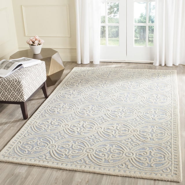SAFAVIEH Cambridge Leslie Geometric Area Rug in a bright room with light wood flooring, featuring hand-tufted wool with textured high/low loop and cut piles in cream and pale blue geometric medallions, styled with a patterned bench and metallic side table, ideal for adding classic texture to home decor.