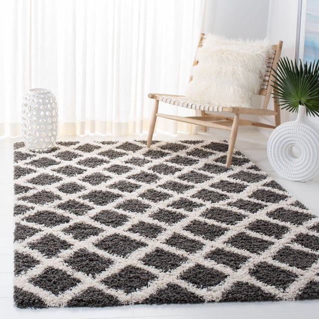 Safavieh Layla Geometric Plush Shag Area Rug with a diamond pattern in dark gray and off-white, shown in a bright room with sheer curtains, a wooden chair with a fluffy white cushion, and white ceramic decor, designed for durability in high-traffic home or office areas and suitable for adding texture and warmth to contemporary spaces.