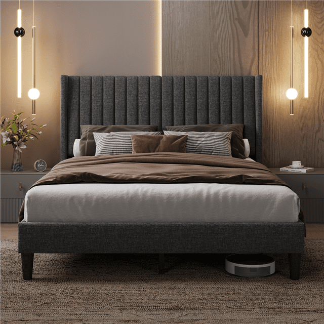 Fullfurnique Upholstered Bed Frame with Wing Side and Channel Headboard, Queen, Dark Gray, featuring a queen-sized dark gray linen upholstered platform bed with vertical channel tufting on the winged headboard, brown and striped pillows, and bedding, set in a modern bedroom with wood panel wall, pendant lights, nightstands, and a robotic vacuum underneath, built with sturdy wooden slats and legs for mattress support.