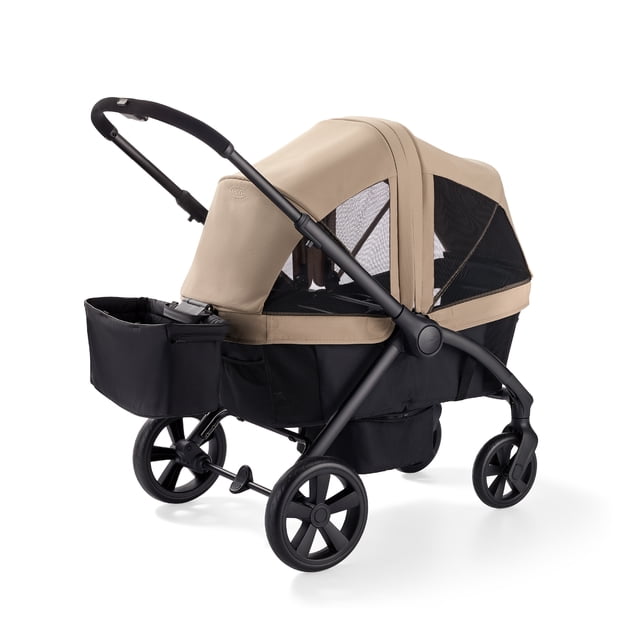 Graco Ready2Roll Stroller Wagon in beige and black with mesh sides, adjustable UV 50 canopy, compact lightweight frame, four all-terrain wheels with rear suspension, rotating push-pull handle, and black storage basket, seating two children comfortably.