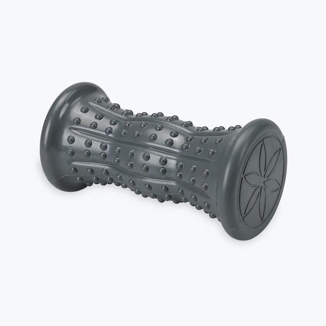 Gaiam Restore Hot/Cold Foot Massage Roller in grey with raised nodules and ergonomic contour to fit the foot arch, shown at a 3/4 angle on a white background. Designed to relieve plantar fasciitis and heel spurs, it supports hot or cold therapy to ease foot pain and improve circulation. The ends have a flower pattern embossing. Also suitable for general foot muscle relaxation.