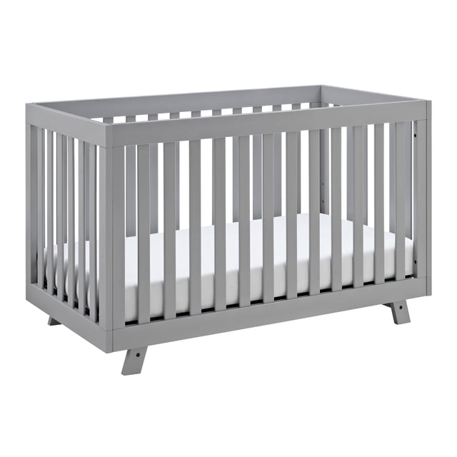 Storkcraft Beckett 3-in-1 Convertible Crib in grey with vertical slats and white mattress, shown from a 3/4 angle, made of pine and engineered wood, featuring adjustable mattress support and convertible design for baby, toddler, and daybed use in nursery.