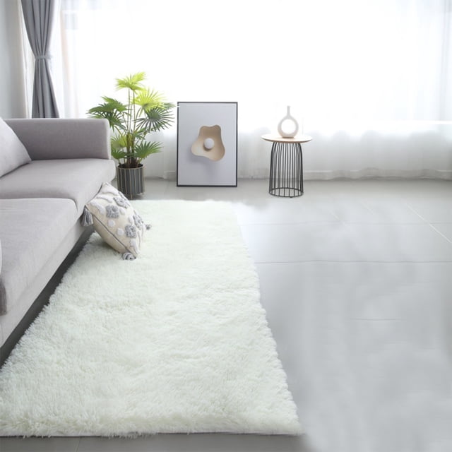 TNDBKQWR Runner Rugs for Hallway Bedside Runner Rug Indoor Rug Area Rug Soft Rugs for Bedroom, 60x200cm. A long, plush white runner rug placed in a modern living room with a grey sofa, decorative pillow, and minimalist decor. The rug features a soft, fluffy texture and a non-slip rubber backing, suitable for bedrooms, hallways, or entryways. Its versatile design complements various furniture styles and is easy to clean by hand or with a damp cloth.