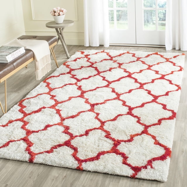 Safavieh Barcelona Anabelle Geometric Shag Area Rug with a white plush shag pile and red Moroccan quatrefoil tile pattern, placed on light wood flooring in a bright room with white curtains, a bench with a throw and books, and a small round table with a flower pot, suitable for adding warmth and style to living spaces.