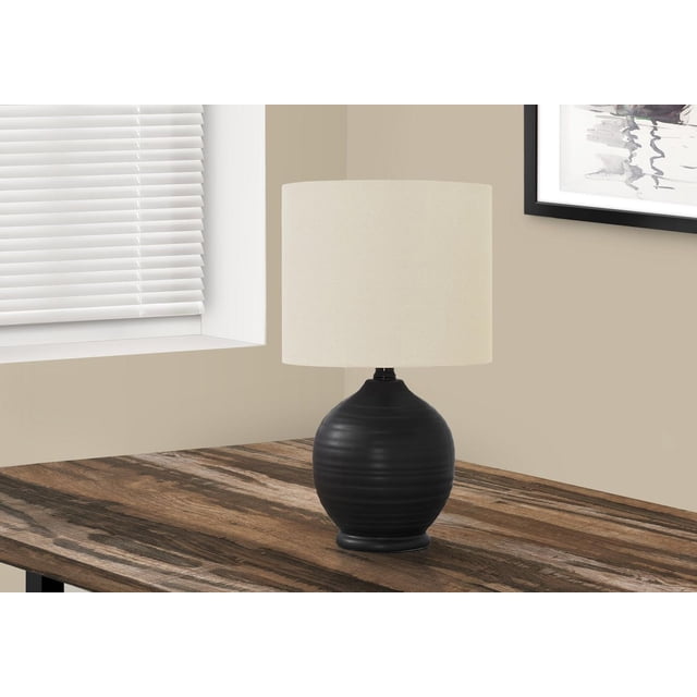 Monarch Specialties Lighting 17"h table lamp with a black ceramic rounded teardrop base featuring subtle horizontal texture and an ivory linen drum shade, placed on a rustic wood table near a window with white blinds and beige walls, suitable for living rooms or bedrooms.