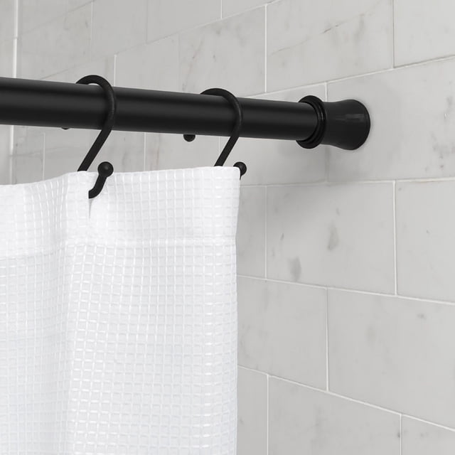 Mainstays Adjustable Tension Shower Curtain Rod in matte black finish mounted on white marble tile wall, holding a white textured shower curtain with black hooks. The rod adjusts from 50 to 86 inches and installs tool-free without wall damage, suitable for rental homes and apartments.