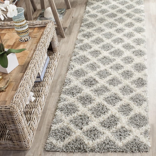 Safavieh Layla Geometric Plush Shag Area Rug runner in light grey and cream diamond pattern on light wood floor beside a wicker console table, made with durable synthetic fibers and a soft, dense texture suitable for high traffic home or office areas.