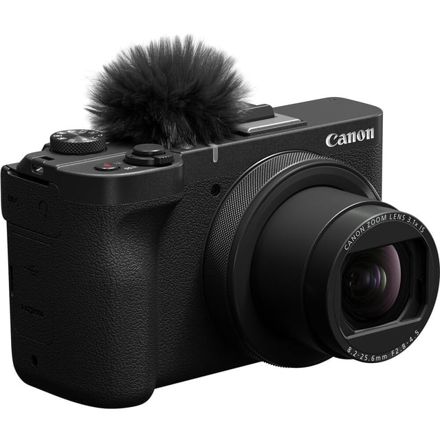 Canon PowerShot V1 Digital Camera in a 3/4 front view with a black textured body, extended 16-50mm F2.8-4.5 wide-angle zoom lens, top control dials, and a furry windscreen on the built-in microphone, suitable for vlogging, live streaming, and continuous 4K60P video recording.