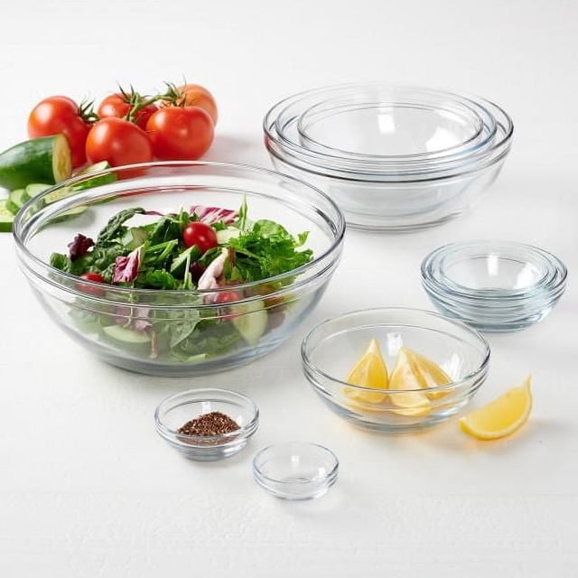 Anchor Hocking 10pc Mixing Bowl Set with clear glass bowls in various sizes, including a large bowl containing fresh salad, smaller bowls holding lemon wedges and spices, arranged on a white surface with fresh tomatoes and cucumber, featuring thick rims, nesting design, and dishwasher and microwave safe glass.