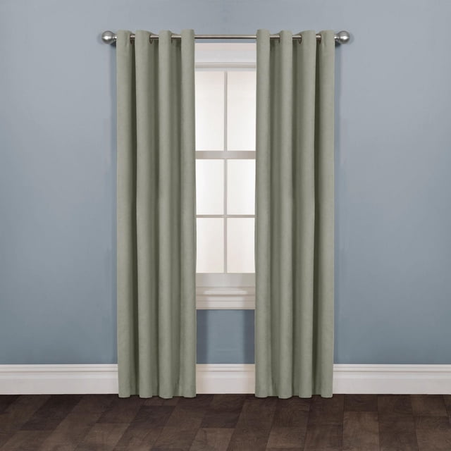 Mainstays Faux Suede Drapery Grommet Window Curtains Panel in muted sage green polyester with a matte finish, hanging on a silver metal rod over a white-trimmed window in a room with light blue walls and dark wood floor, featuring easy-install grommet rings and suitable for room darkening.