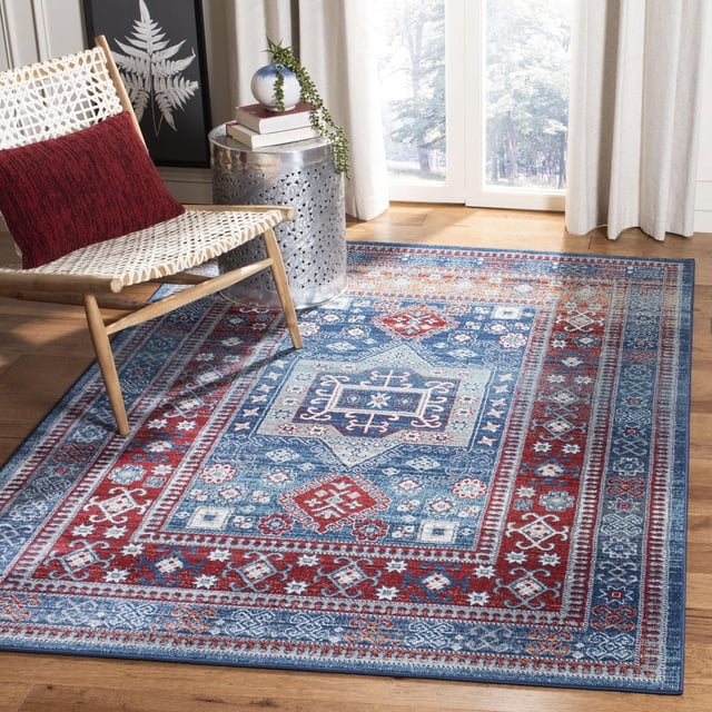 Safavieh Kazak Caymen Tapis Géométrique pour Aire Affichant des motifs Géométriques et Floraux Complexes en Couleurs Bleu Vif, Rouge et Crème, Fabriqué à Partir de Fils Synthétiques Durables avec un Poil Coupe Modérée pour le Confort, Placé sur un Plancher de Bois Franc à Côté d'Une Chaise Tressée avec un Coussin Rouge et une table d'Appoint Décorative Argentée avec des Livres et une Plante, Près d'Une Fenêtre avec des Rideaux Beiges. Il Est Aussi Idéal pour Améliorer la Symétrie Décorative et une ambiance Palatiale dans la Déco de la Maison.