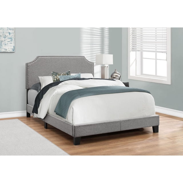 Monarch Specialties Bed, full size platform bed frame upholstered in grey linen-look fabric with chrome nail head trim and arched cut-out headboard silhouette, supported by black solid wood legs, placed in a bright bedroom with light hardwood flooring and white window blinds.