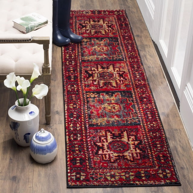 SAFAVIEH Vintage Hamadan Edin Traditional Area Rug with richly colored Persian-style geometric motifs in red, black, and gold tones, displayed as a runner on wood flooring beside a beige tufted bench, blue rain boots, and ceramic vases with white calla lilies, ideal for adding vintage charm to hallways or entryways.