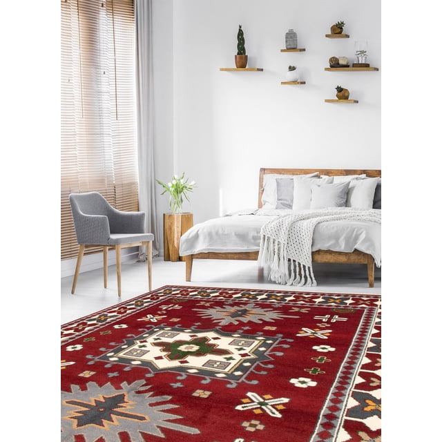 ECARPETGALLERY 100% Wool Traditional Indoor Area Rug with bold geometric Persian Kazak-inspired patterns in red, cream, green, and grey, displayed in a bright bedroom with a wooden bed dressed in white linens, a grey upholstered chair, and floating wooden shelves holding small plants and decor, ideal for entrance, bedroom, living, or dining rooms.