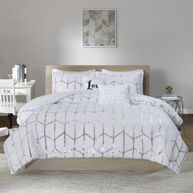 Home Essence Apartment Arielle Duvet Cover Set on a bed with a light wood headboard in a modern bedroom. The white duvet cover features a silver metallic geometric pattern with two matching shams. Included are two embroidered decorative cushions, one square with silver dots and one oblong with 'Love' typography. The set is styled with a neutral wall, geometric framed art, a white desk with books and chair on one side, and a round side table with a plant and books on the other. The floor has a light rug over wood flooring.