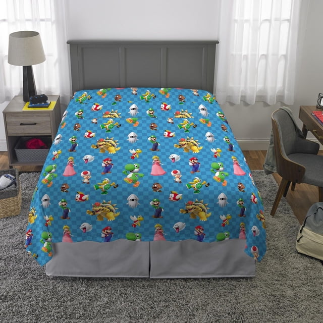 Super Mario "All The Players" full sheet set featuring a blue checkered pattern with Mario, Luigi, Princess Peach, Yoshi, Bowser, Toad, Goomba, Koopa Troopa, Boo, and Blooper characters, made of 100% polyester microfiber, machine washable, designed to fit a standard full bed, displayed on a bed with a gray headboard in a child's room.