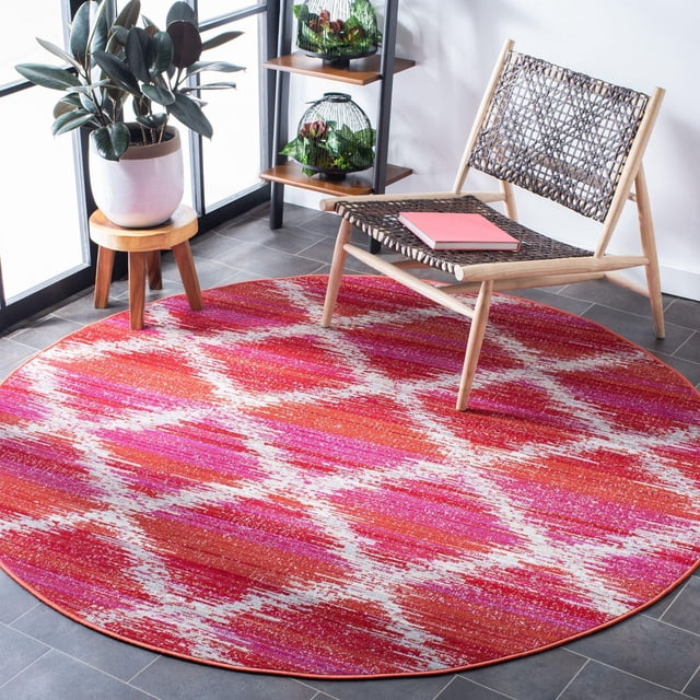 Safavieh Montage Tapis d'Extérieur Géométrique Melva, Rond avec un Motif Géométrique dans des Tons Rouge, Rose et Blanc, Tissé Mécaniquement pour la Durabilité Extérieure, Exposé sur un Plancher de Carreaux Gris à Côté d'Une Chaise en Bois Tressée et d'Un Petit Tabouret en Bois avec une Plante en Pot, Convient pour Améliorer les Espaces de Vie Extérieurs.