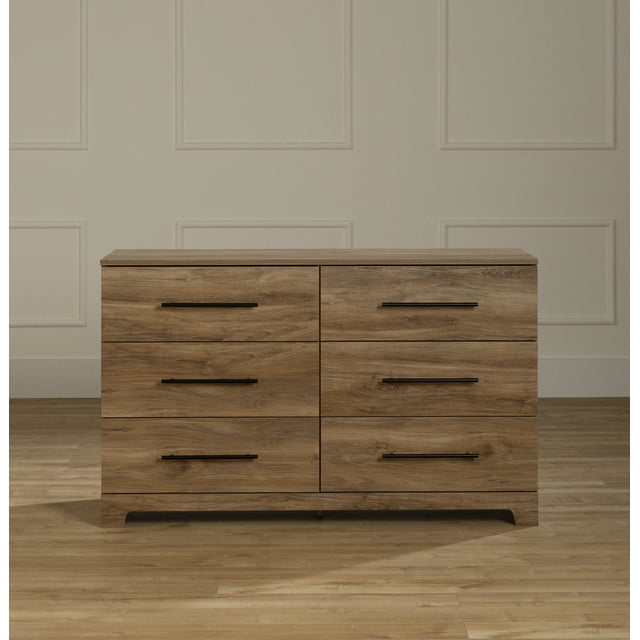 South Shore Barcelo 6-Drawer Dresser for Adult in natural mango finish, front view showing six spacious drawers with black metal handles and a rounded base, set on hardwood flooring against a beige paneled wall, designed for bedroom storage and also suitable for organizing linens or accessories.