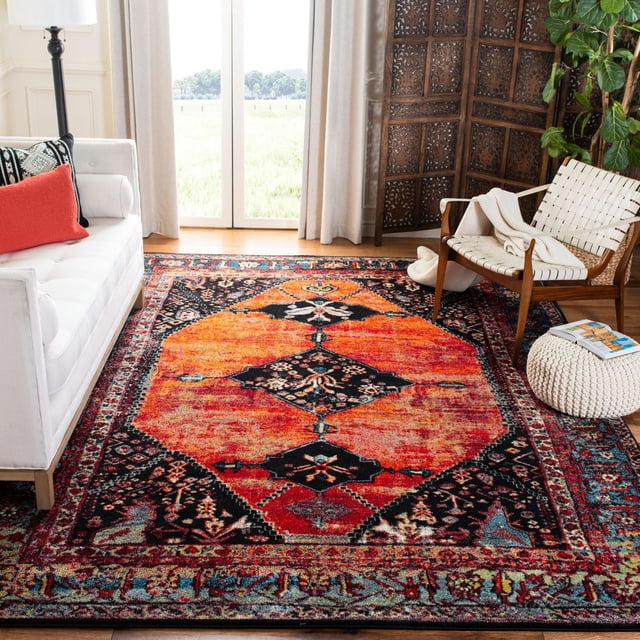 Safavieh Vintage Hamadan Samia Tapis Traditionnel pour Aire dans un Salon Lumineux avec un sofa Blanc Accentué d'Un Coussin Rouge et d'Une Chaise Blanche Tissée avec un Jeté beige, Placé Près d'Un Écran en Bois Sculpté et d'Une Plante Verte, Présentant un design de Style Persan avec des Couleurs orange, Noir et Rouge Vibrantes et des Motifs Floraux Détaillés, Idéal comme Tapis d'Accent Décoratif.