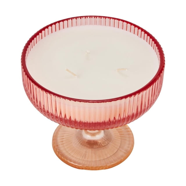 Anko Citrus Spritz Candle in a ribbed glass pedestal tumbler with a red upper bowl and amber base, containing three wicks and white wax, suitable for indoor home décor and often used to add a fresh citrus aroma to living spaces.