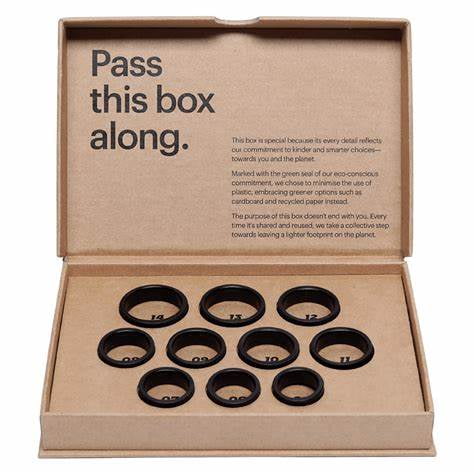 Ultrahuman Ring AIR Sizing Kit with 10 black mock rings sized 5 to 14 arranged in a recycled cardboard box featuring eco-friendly messaging inside the lid, designed for accurate smart ring sizing and sustainable packaging.