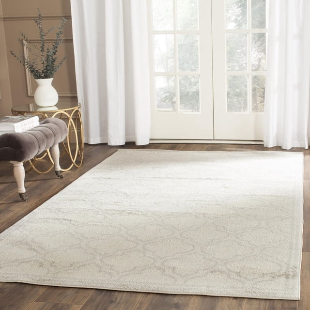 Safavieh Amherst Wilson Tapis Géométrique en Teinte Neutre Légère avec un Subtil Motif de Treillis Géométrique, Tissé Mécaniquement en Polypropylène durable pour un Entretien Facile dans les Espaces Intérieurs Très Passants, Montré sur un Plancher de Bois Franc Foncé dans une Pièce Lumineuse avec des Rideaux Blancs, un Banc Capitonné Gris et une table d'Appoint en Métal Doré avec un vase Blanc et de la Verdure.