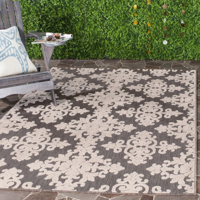Safavieh Cottage Damjan Tapis d'Extérieur Géométrique Floral pour Aire avec Motifs Floraux Crème sur Fond Brun Foncé, Fibres Synthétiques Tissées Mécaniquement pour la Durabilité, Montré sur un patio en Pierre à Côté d'Une Chaise en Bois avec Coussin, Convient aux Zones et patios Extérieurs à Fort Passage.