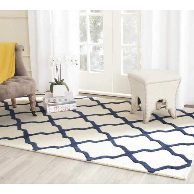 Safavieh Cambridge Liam Tapis Géométrique pour Aire avec Fond Crème et Motif Treillis Bleu Marine, Laine Tuftée à la Main avec Poil Couper Peluche et Poil en Boucle Texturé Haut/bas, Exposé sur Plancher de Bois Clair dans une Pièce Lumineuse avec Chaise Rembourrée beige, Jeté Jaune, Orchidée Blanche sur Livres Empilés et Tabouret Bordé de Clous beige, Idéal pour la Déco Moderne de la Maison Ou du Bureau.