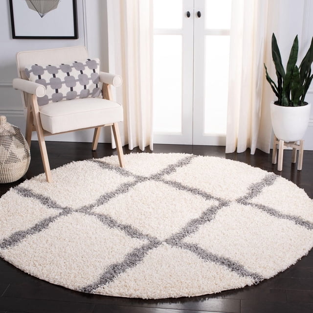 Safavieh Dallas Logan Geometric Shag Area Rug, round with ivory plush polypropylene pile and gray Moroccan tile pattern, placed on dark hardwood floor in a bright room with a cream armchair, patterned pillow, woven basket, and potted snake plant by white curtains and glass doors, ideal for adding texture and warmth to accent spaces.