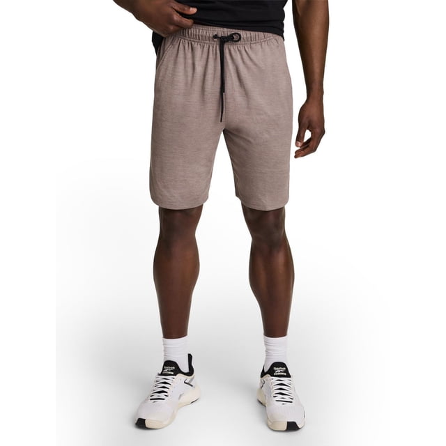 Reebok Shorts Delta Core pour Hommes en taupe Atténué, Vue avant d'Un Modèle Masculin de la Taille à Mi-Cuisse, Fabriqué en Tissu jersey Doux avec 89 % polyester et 11 % Élasthanne, Doté d'Une Taille Élastique avec Cordon de Serrage Noir et Poches Latérales, Assorti aux Chaussures Athlétiques et Chaussettes Reebok Blanches, Idéal pour l'Entraînement Ou les Tenues Décontractées.